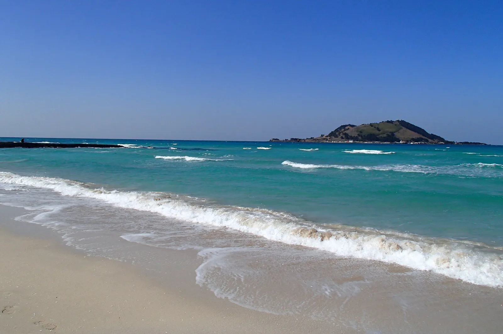 Clear blue water and dark volcanic rock at Hyeopjae Beach on western Jeju
