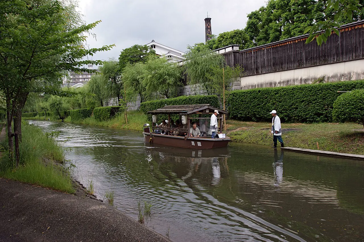 Traditional boat moving along a green canal in Fushimi's sake district