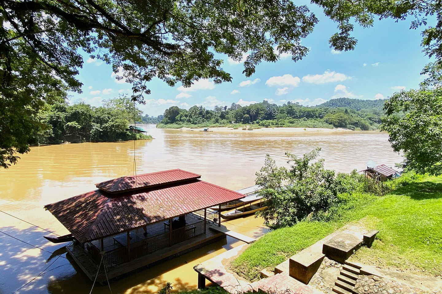 Brown river, boats and a shaded landing at Kuala Tembeling